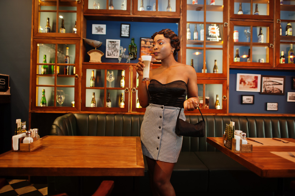 mulher posa para foto em frente a estante decorada e móveis instagramáveis em um bar