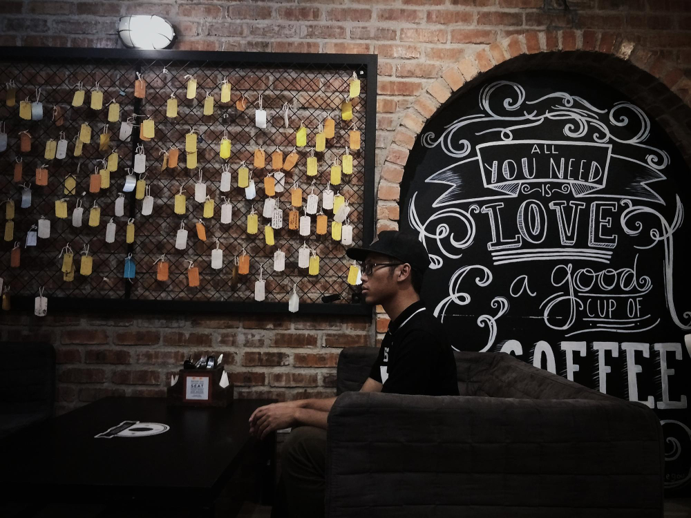 homem aguardando pedido em café com painel de recados interativo