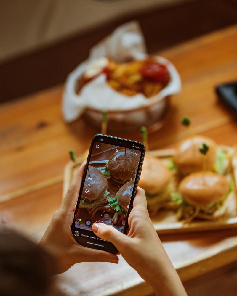 close em mãos segurando smartphone tirando foto de hamburguers 