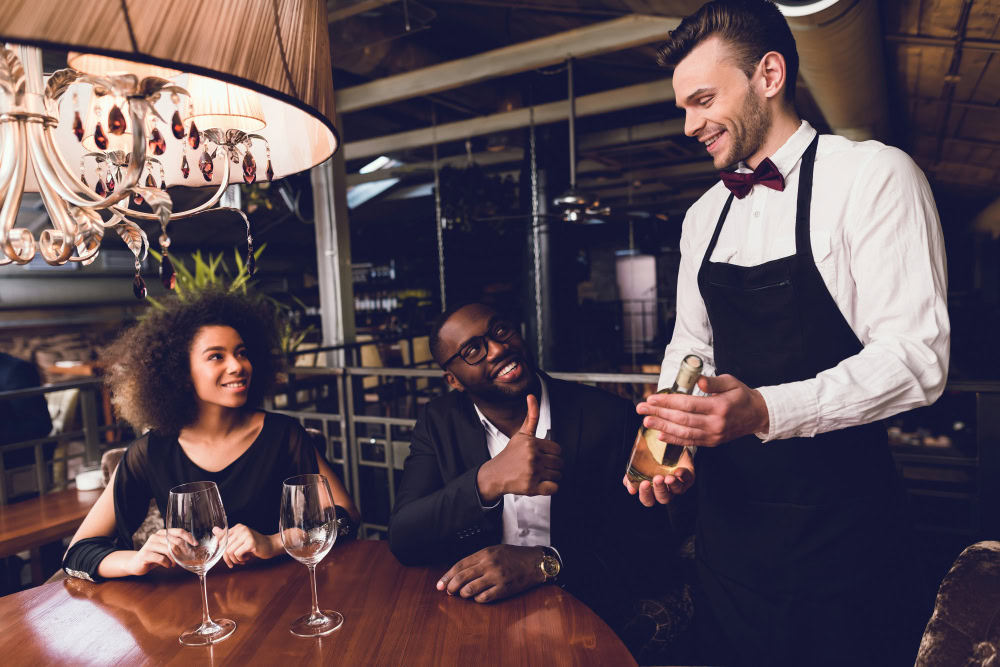 garçom servindo vinho a um casal em um bistrô