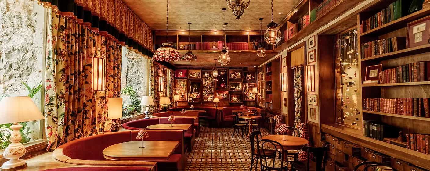 Salón de Mata Città, con bancos de terciopelo rojo, estanterías de libros y lámparas colgantes