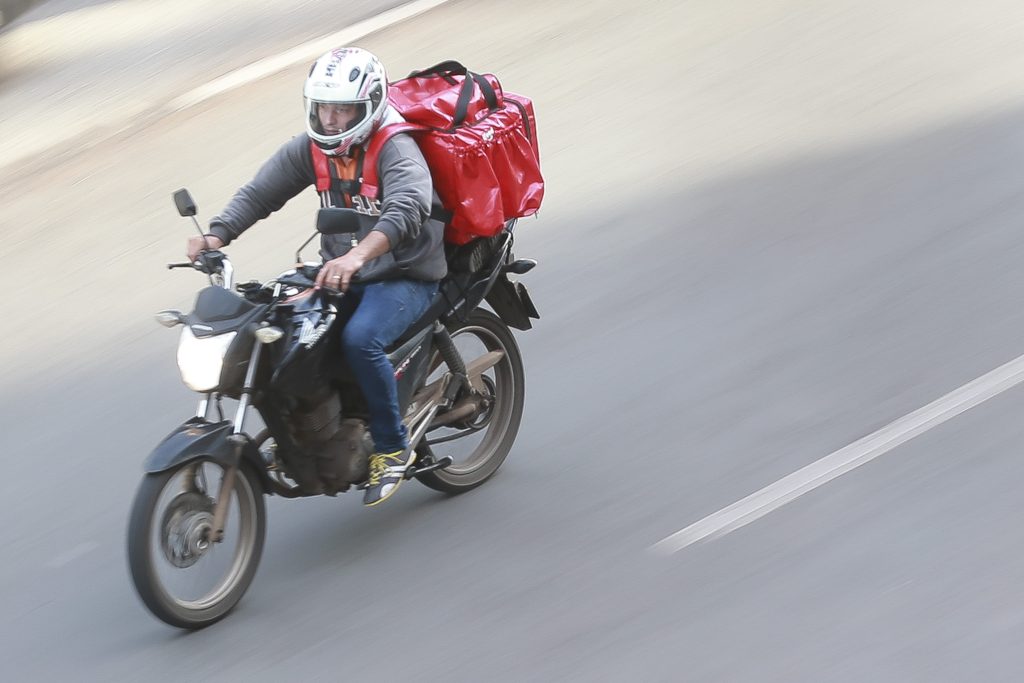 Entregador de delivery de marmitas dirigindo moto